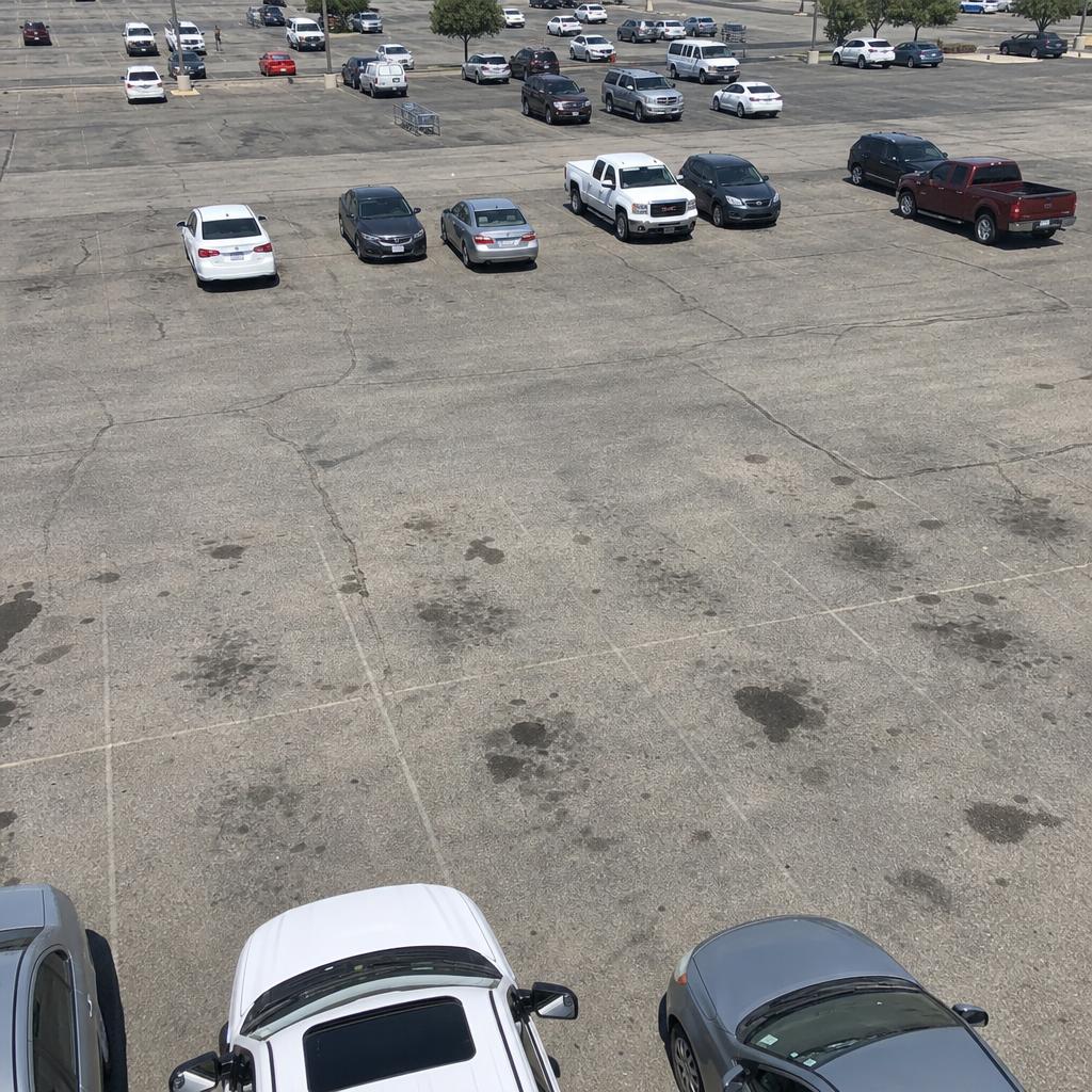 Sun-bleached commercial parking lot with faded lines and cracked asphalt before sealcoating